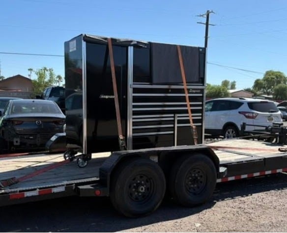 Black enclosed livestock trailer with dual axles parked in a lot with vehicles in background